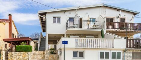 A two-story building with a balcony, a stone staircase, and a sign indicating a parking area.
