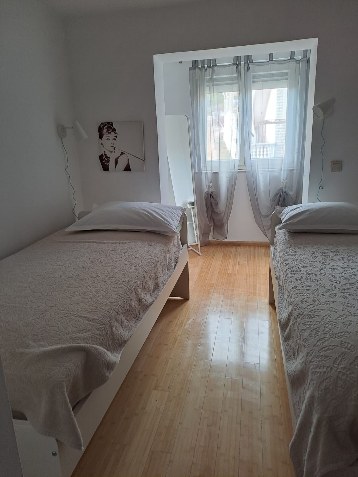 Makuuhuoneessa on kaksi erillistä sänkyä, ikkuna, jossa on läpikuultavat verhot, seinään kiinnitetty lamppu ja kehystetty taulu.