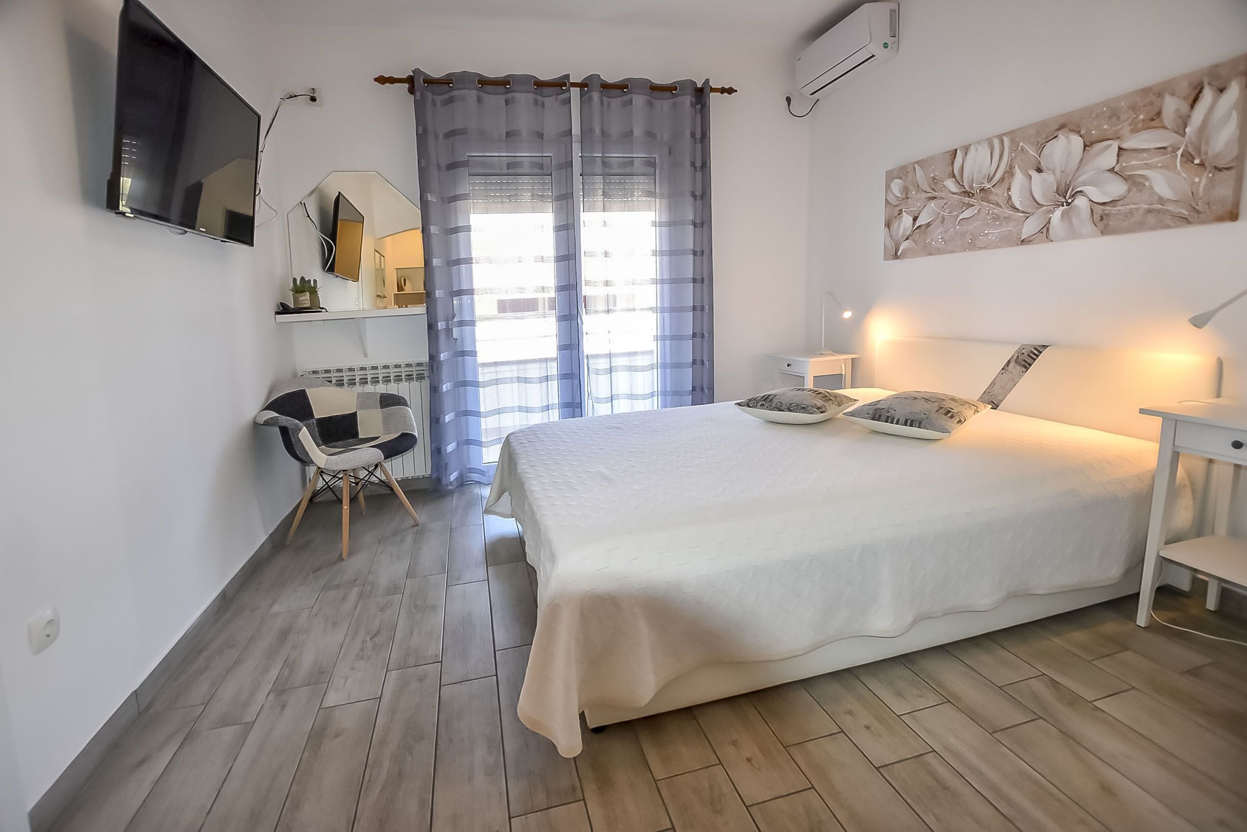 Une chambre à coucher avec un grand lit, un bureau, une chaise, une télévision et une fenêtre avec des rideaux.