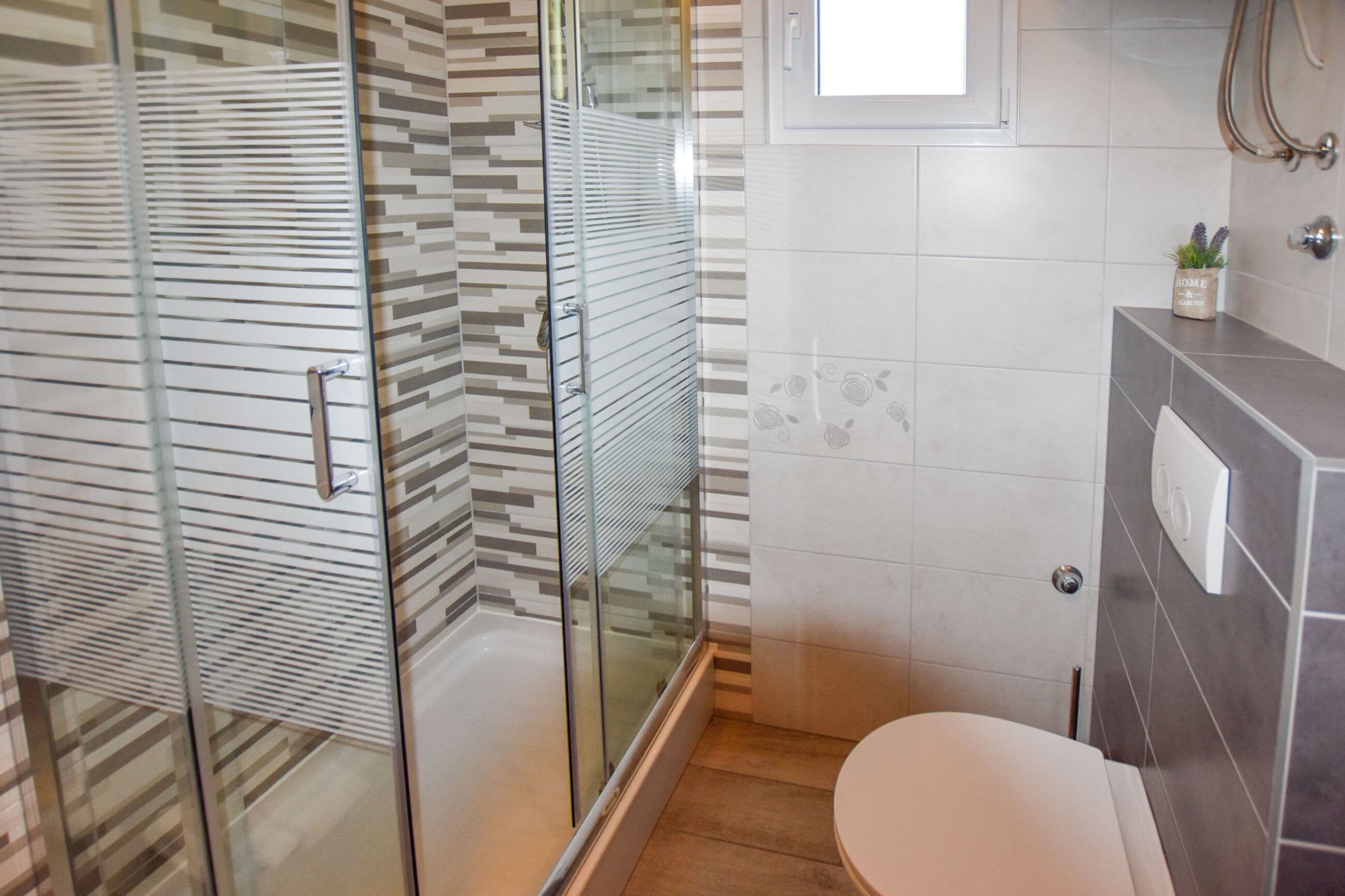 Un baño moderno con cabina de ducha de vidrio, inodoro y lavamanos con dispensador de toallas.