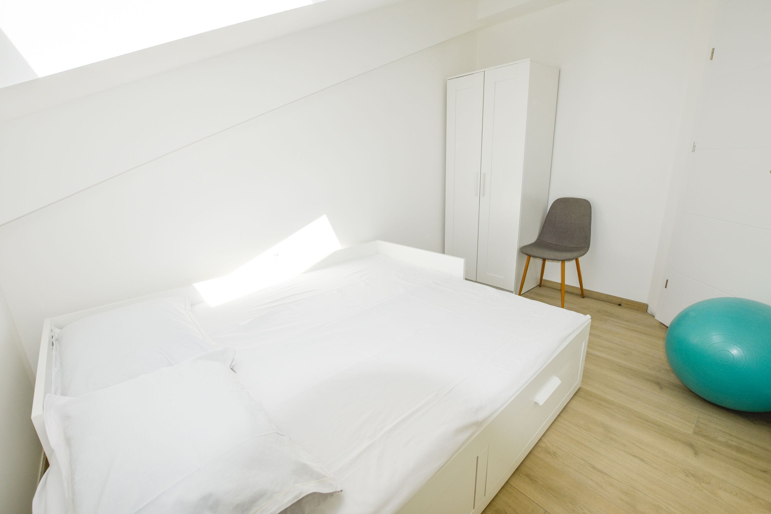 Een kamer met een bed, een kledingkast, een stoel en een grote fitnessbal.