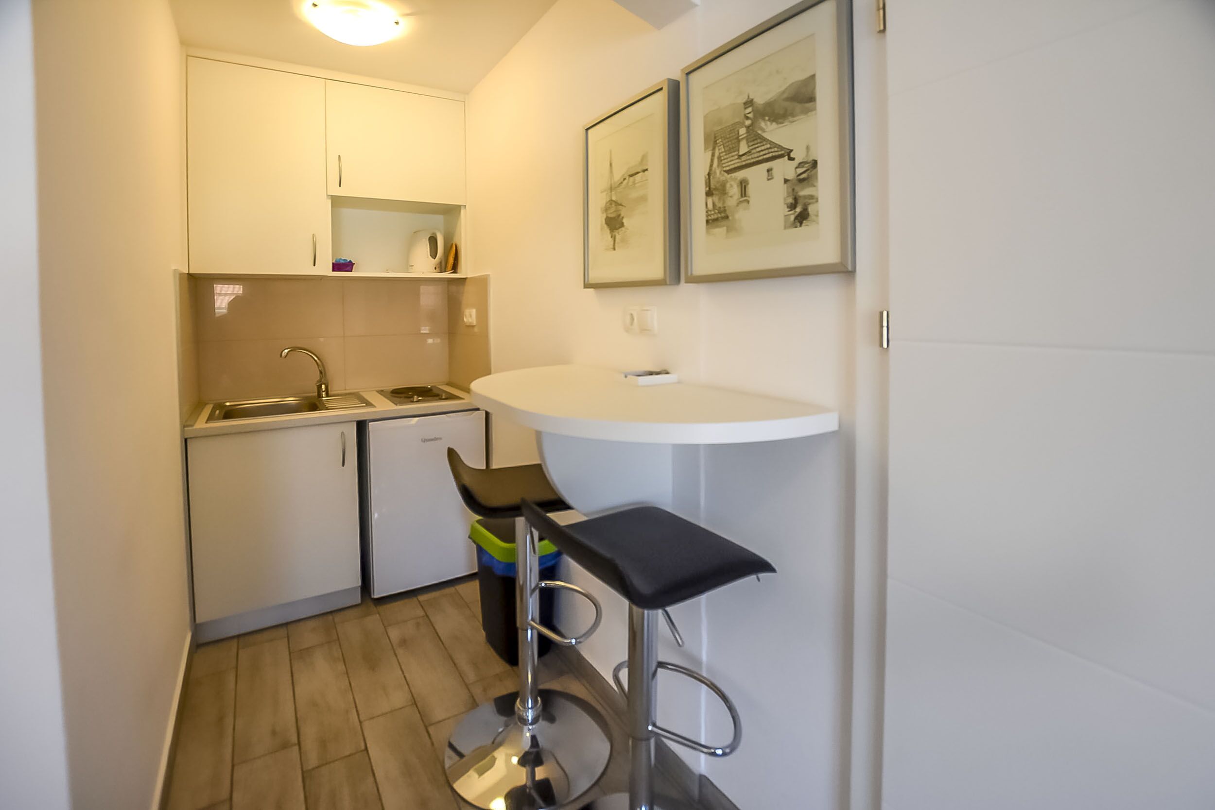 Et lille køkken med vask, minikøleskab og en barstol.