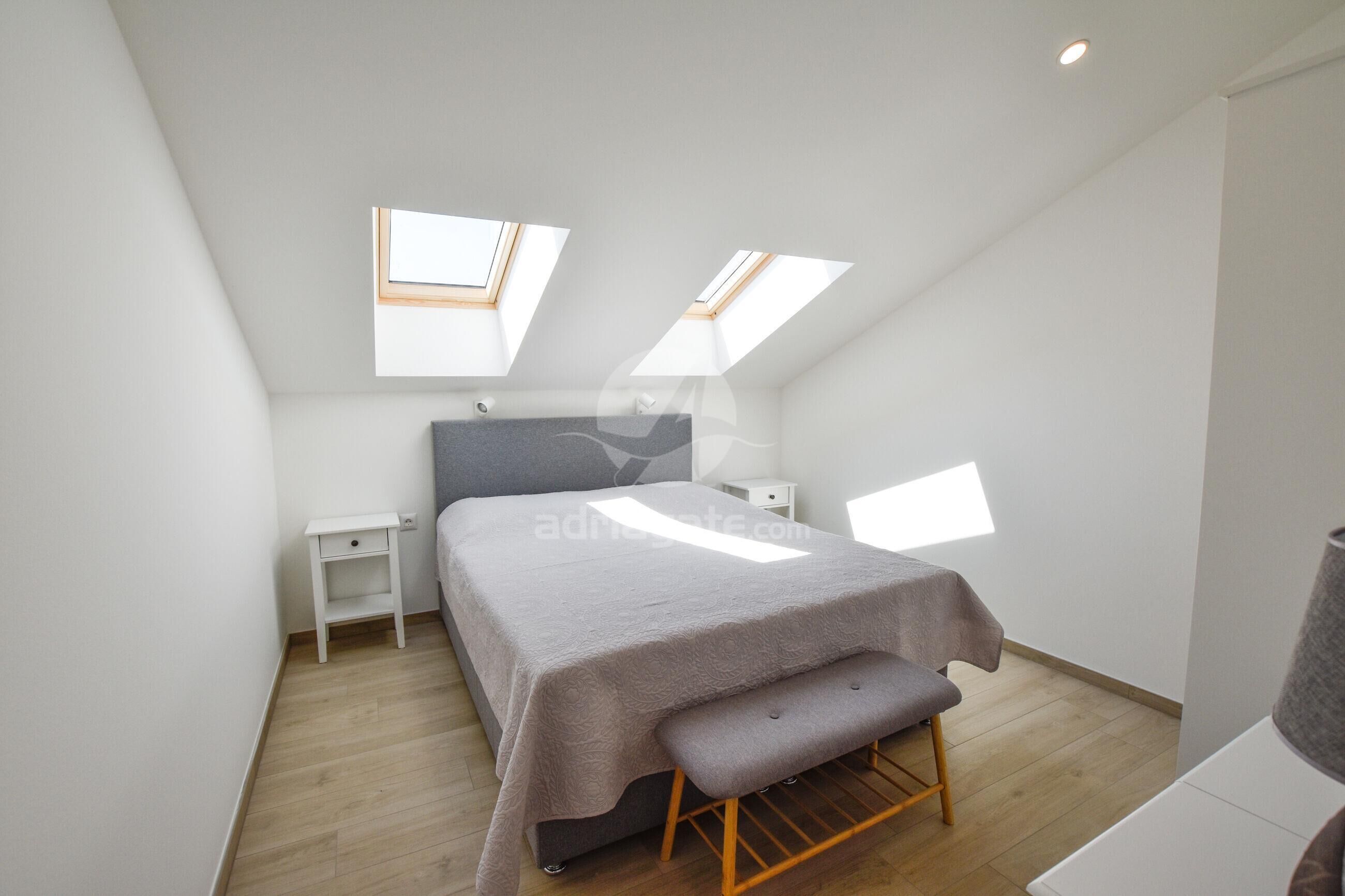 Une chambre à coucher avec un lit, une table de chevet, un banc et des fenêtres de toit.