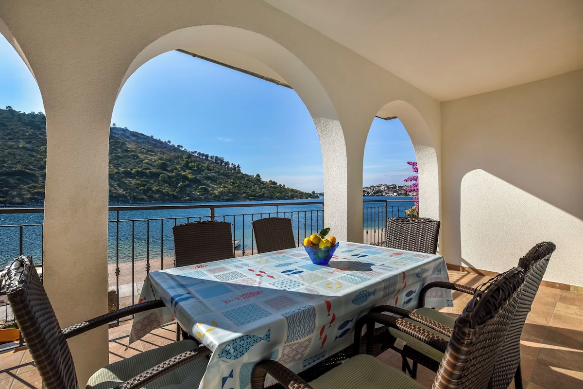 A terrace with a table set for dining, overlooking a lake and hills.