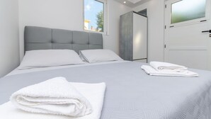 Een moderne slaapkamer met een groot bed, een grijs hoofdeinde, wit beddengoed en uitzicht buiten door een raam.