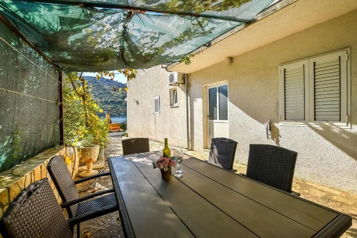 An outdoor patio with a table and chairs, a potted plant, and a view of a mountain.
