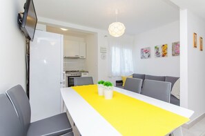A modern kitchen with white cabinets, a built-in oven, and a dining area with a yellow table and grey chairs. - Apartments Milan (Rogoznica)