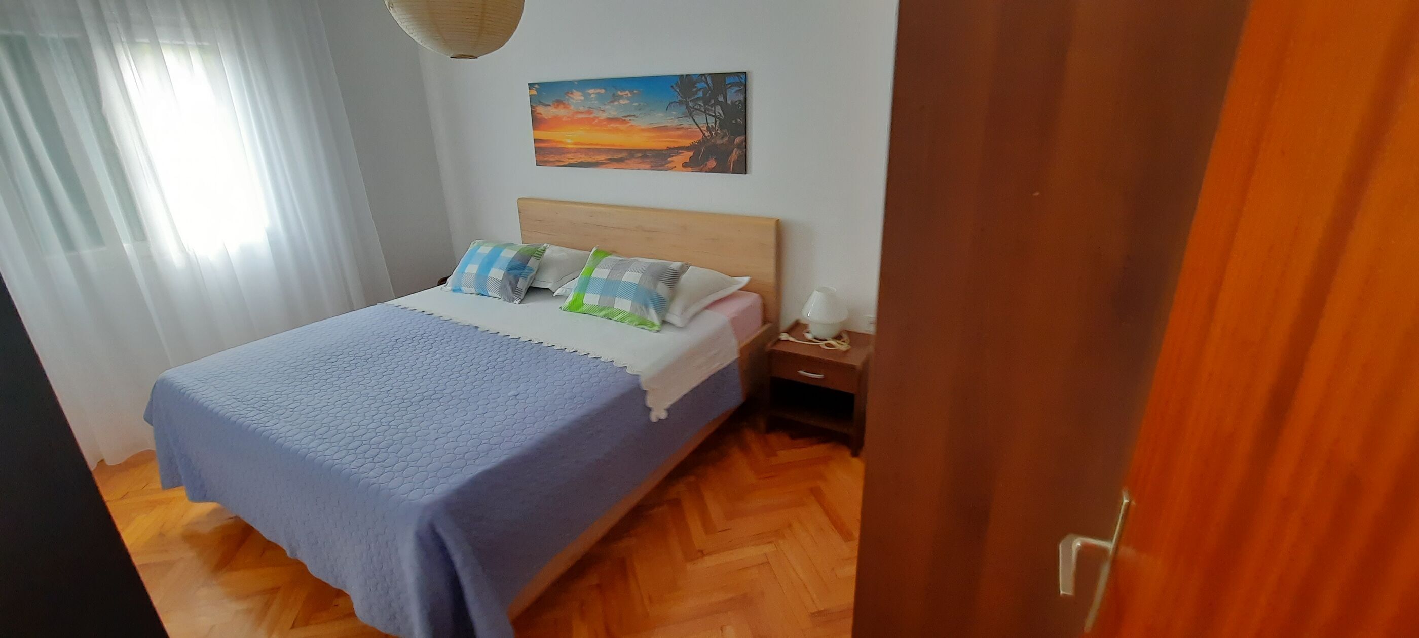 A bedroom with a bed, a nightstand, a lamp, and a painting on the wall.
