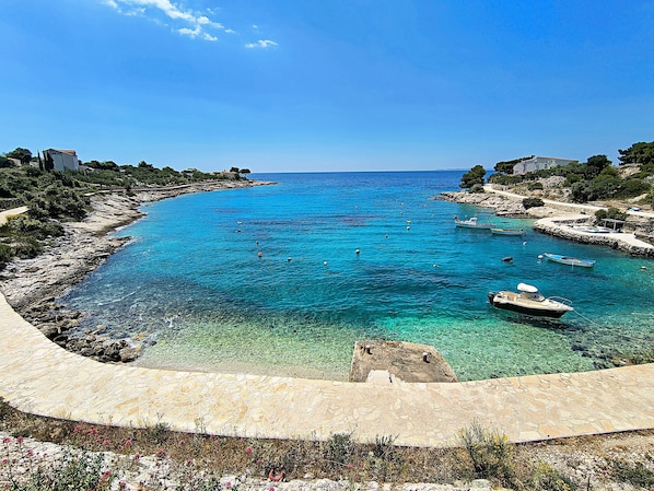 A coastal view with clear turquoise waters, boats, and rocky shores.
