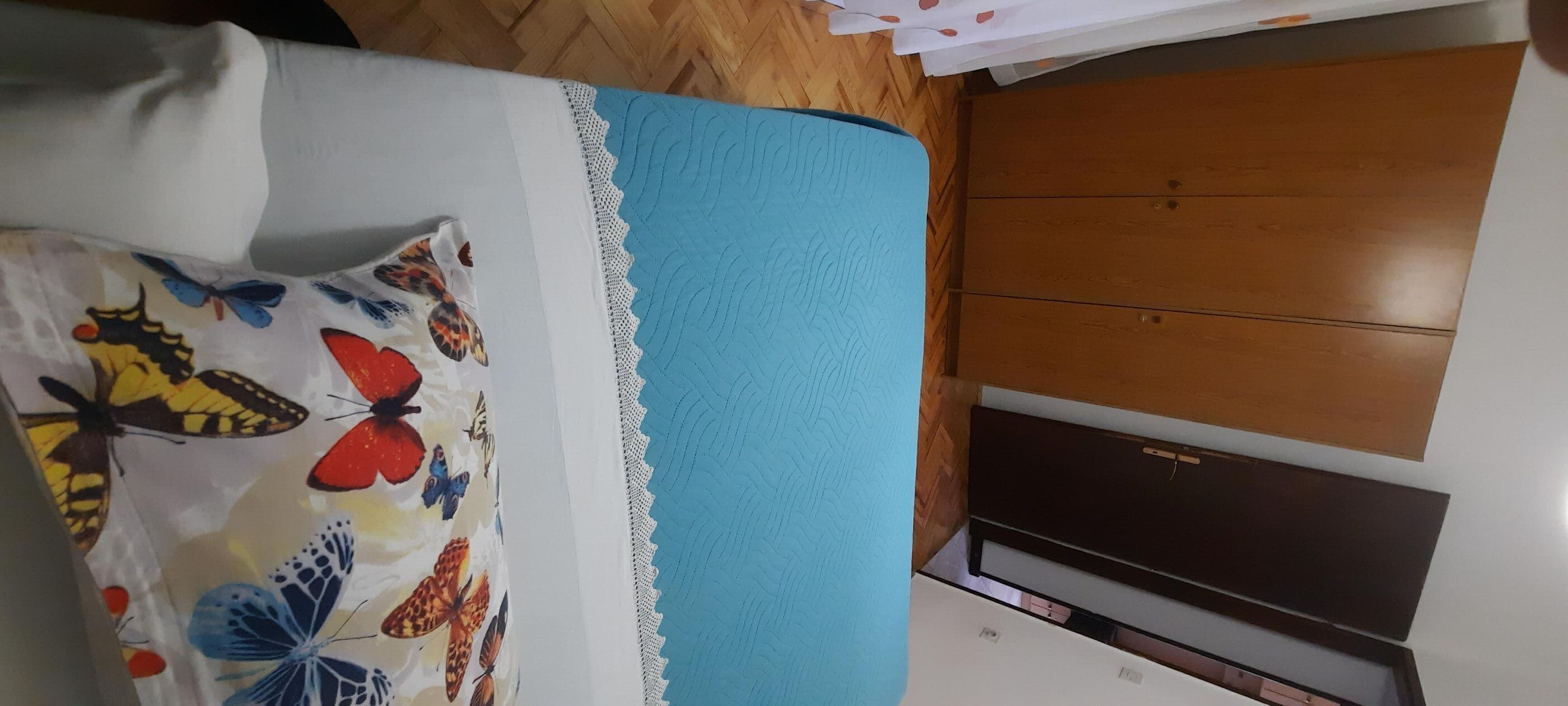 A room with a bed, a blue accent wall, a wooden wardrobe, and a white air conditioning unit.