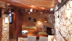 Una habitación acogedora con pared de piedra, techo de madera, una cama con almohadas, una mesa con un control remoto, un ventilador y un televisor.