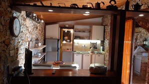 Una cocina rústica con paredes de piedra, techo de madera y una isla central con un hervidor y un bol.