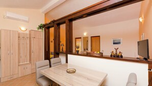Un comedor con mesa y sillas de madera, televisor y mostrador de cocina con armarios y frutero.