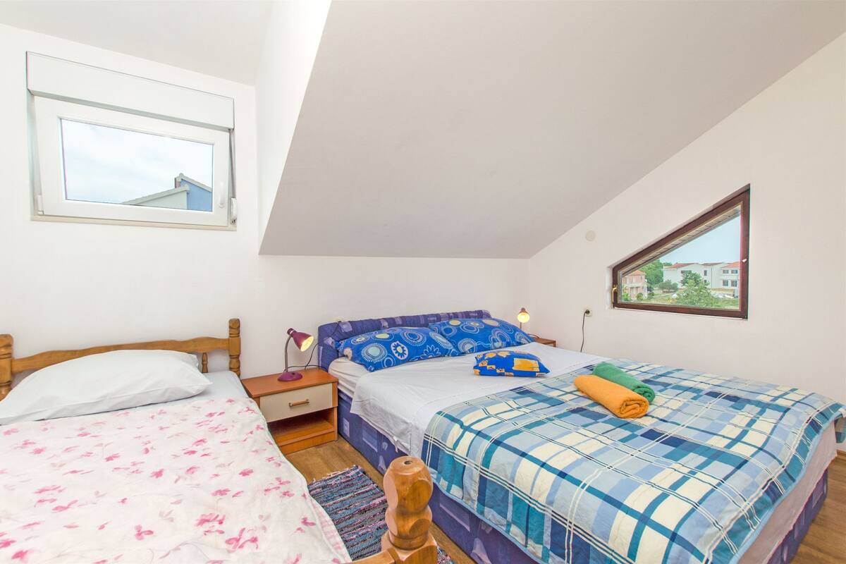 Une chambre avec deux lits, une fenêtre et une table de chevet avec une lampe.