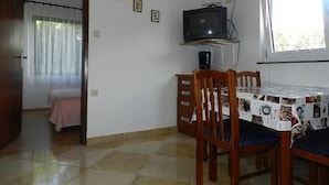 Ein Essbereich mit Tisch, Stühlen, einem Fernseher auf einem Schrank und einem Fenster mit Vorhängen.