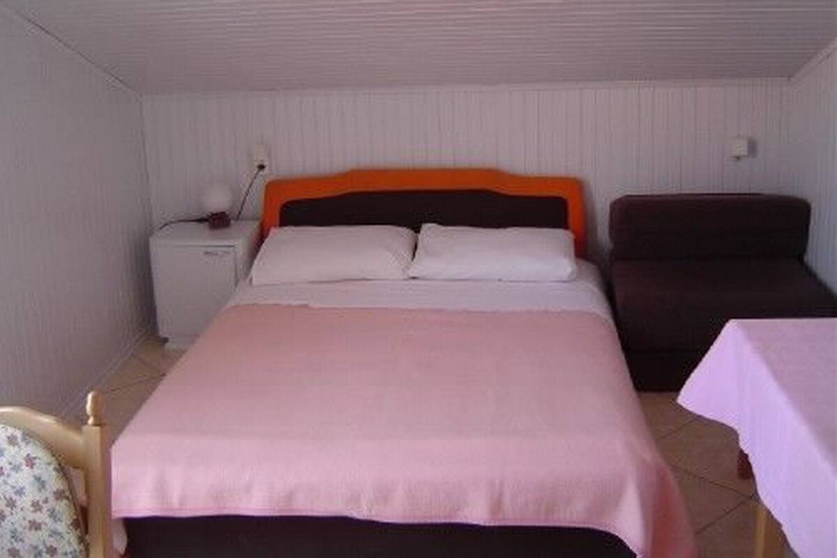 A single bed with an orange headboard, a bedside table, and a chair.