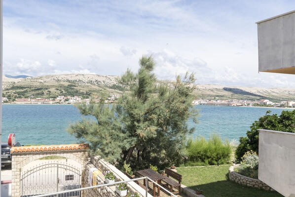 A coastal view with a stone gate, a wooden table and bench, and a large pine tree in the foreground. - Apartments Tina Sea View (Pag)