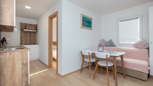 A compact kitchen with a wooden countertop and a sink, a dining area with a table and chairs, and a cozy sleeping area with a bed and pillows. - Mobile Home Sea Turtle (Pasman)