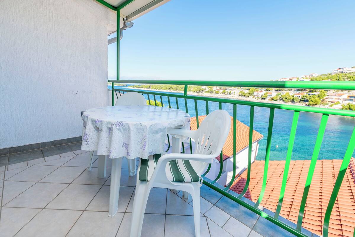 Ein Balkon mit Tisch und Stühlen, der auf ein Gewässer und eine Küstenstadt blickt.