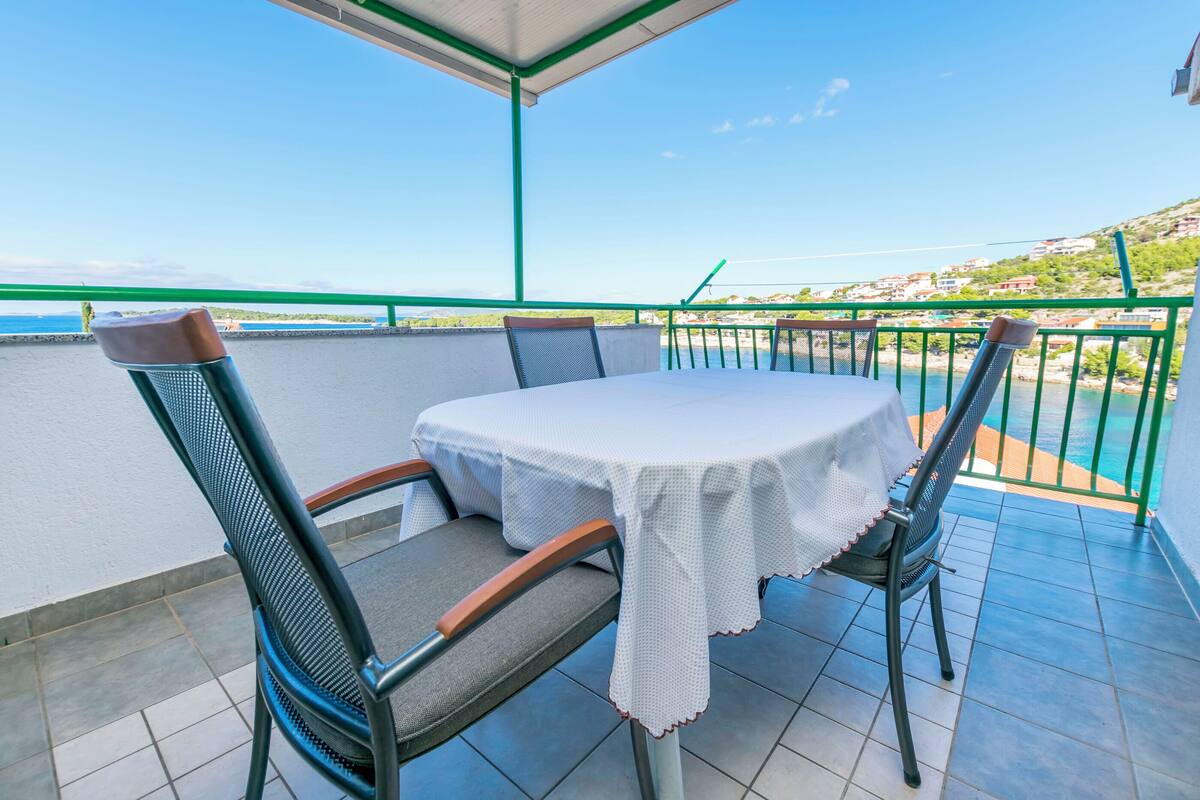 Ein Balkon mit Tisch und Stühlen, mit Blick auf eine Küstenlandschaft und Häuser im Hintergrund.