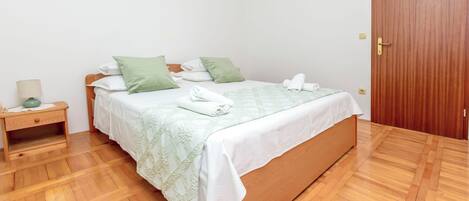 A neatly made bed with a green and white bedspread, a wooden nightstand with a lamp, and a wooden door.