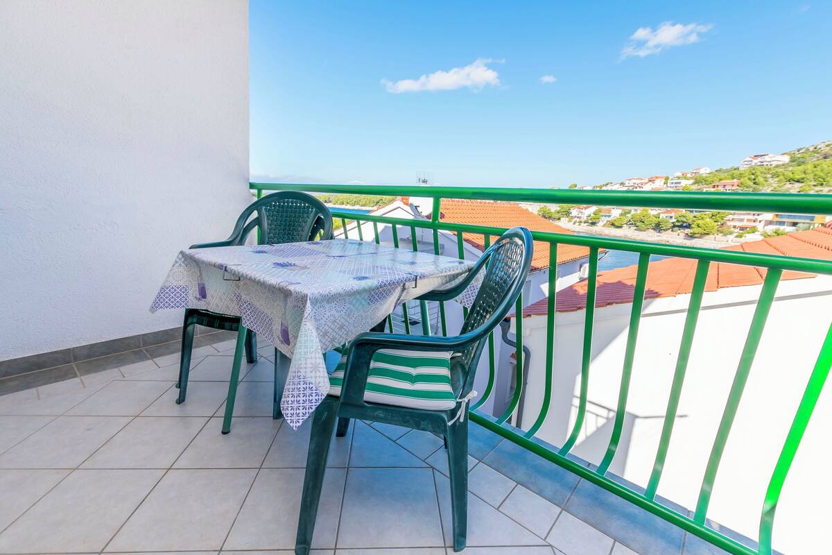 Ein Balkon mit Tisch und Stühlen, einem grünen Geländer und Blick auf eine Hügelkuppe mit Gebäuden.
