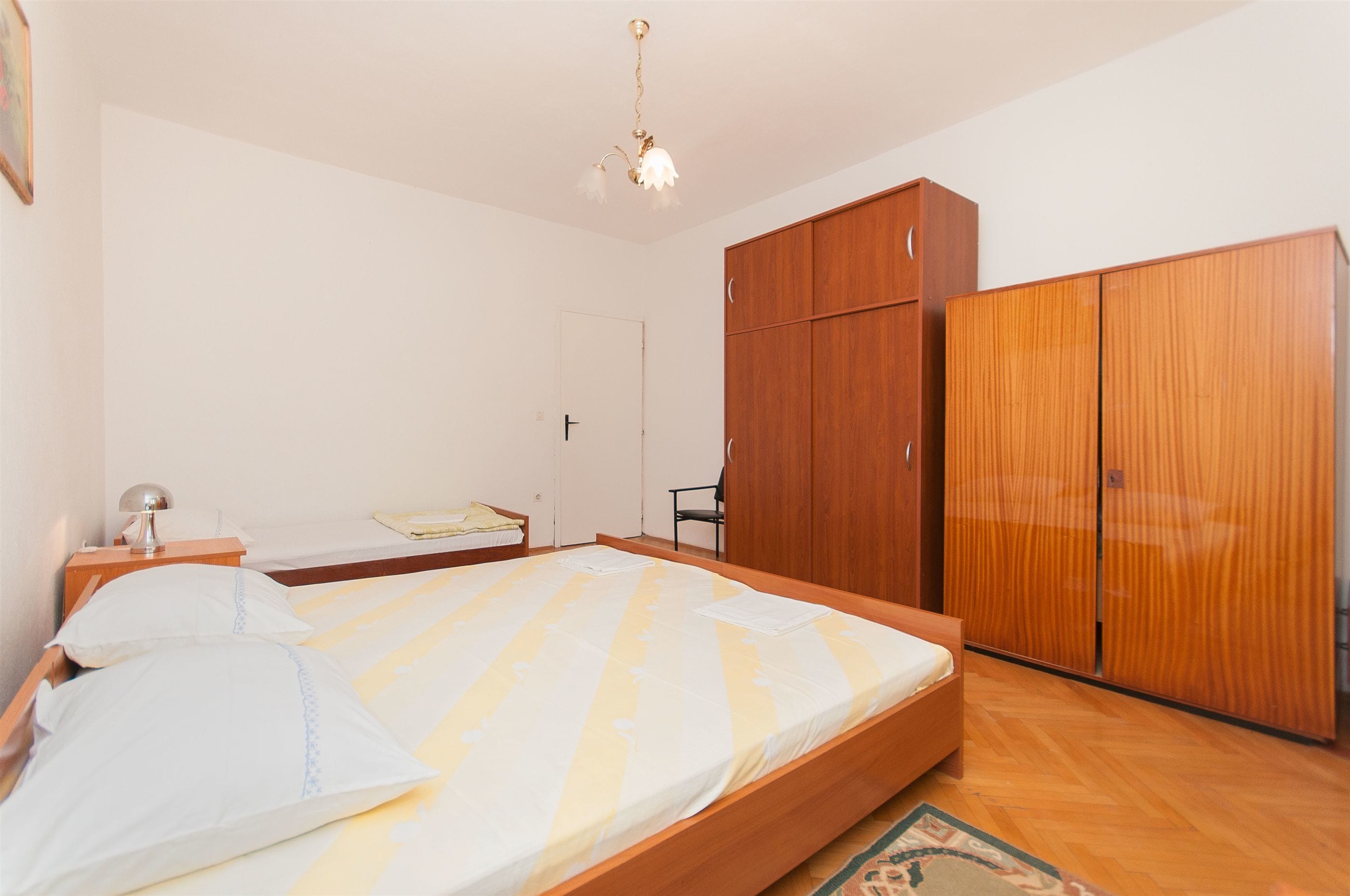 A bedroom with a bed, wooden wardrobe, and a desk with a lamp.