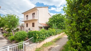 A two-story building with a balcony, surrounded by lush greenery and a paved path. - Apartment Slavko (Biograd)