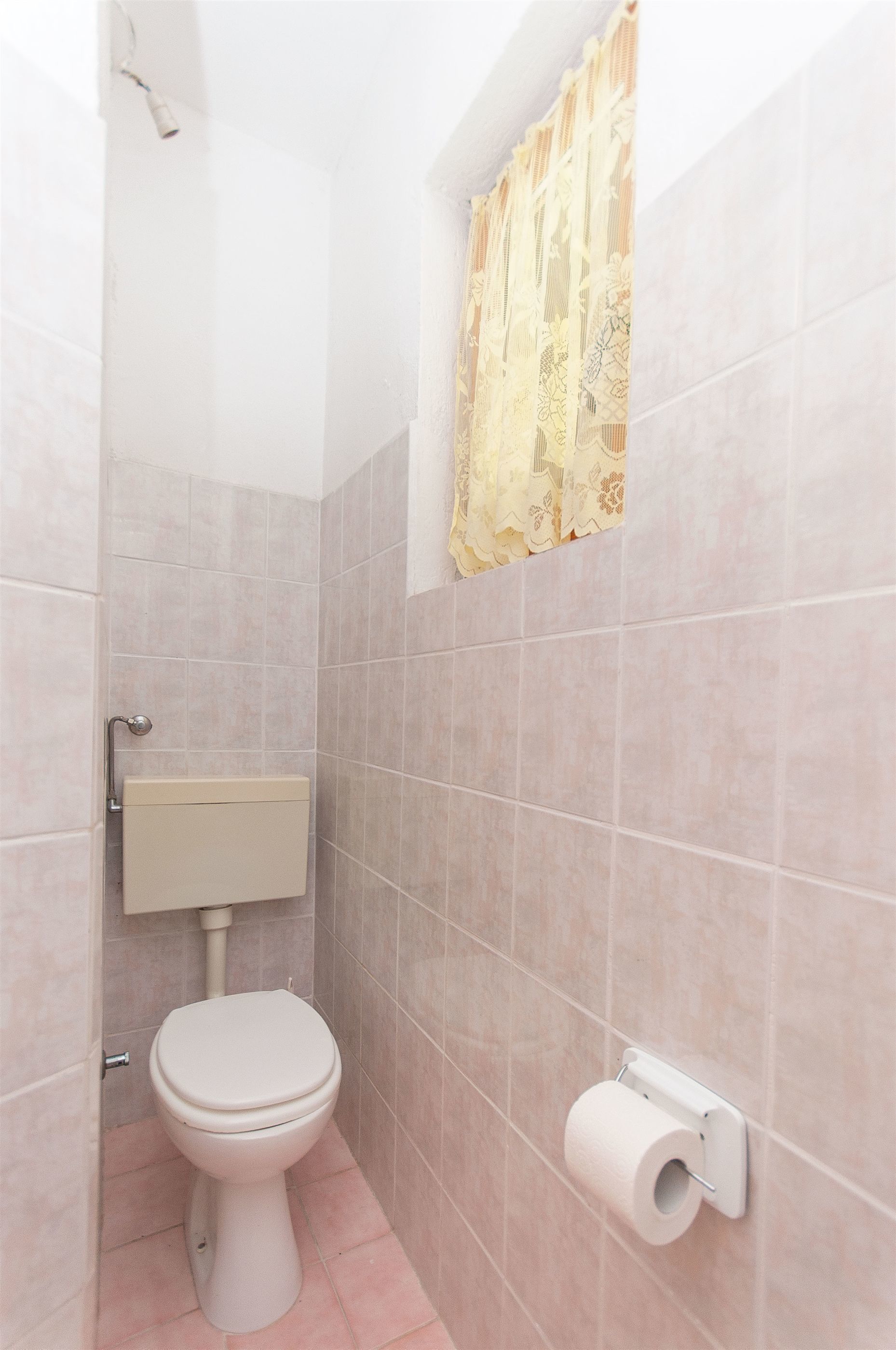 Une salle de bain équipée de toilettes, d’un porte-rouleau de papier toilette et d’un rideau décoratif.