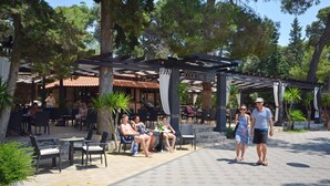 An outdoor seating area with tables and chairs, a covered bar area, and a pergola structure. - Apartment Slavko (Biograd)