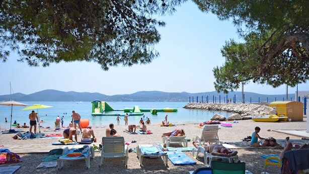 A beach with sun loungers, umbrellas, and a water slide. - Apartment Slavko (Biograd)