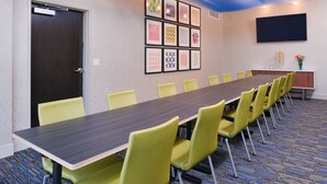 A conference room with a long table and yellow chairs, a door, framed artwork on the wall, and a flat-screen TV. - Holiday Inn Express & Suites Olathe West by IHG (Olathe)