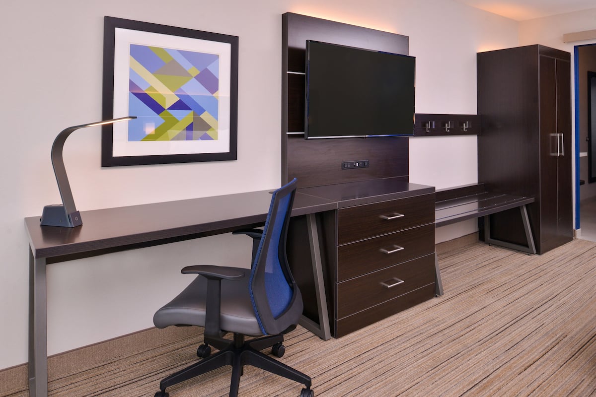 A modern office space with a desk, chair, television, and cabinets.