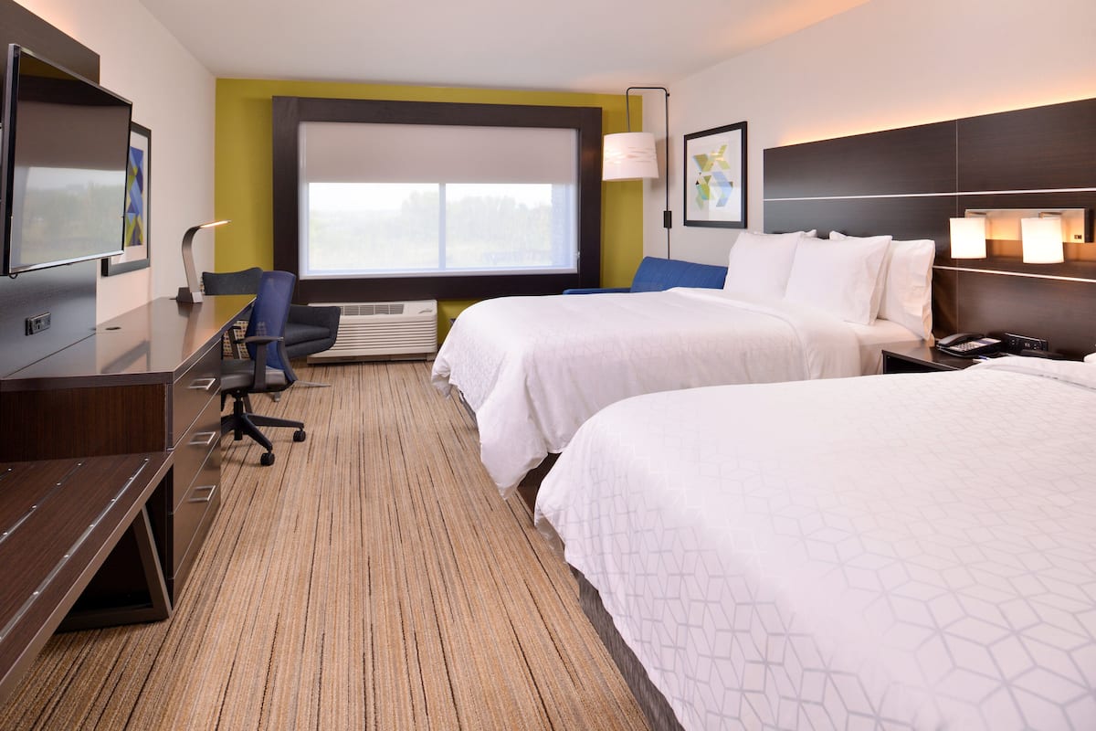 A hotel room with two beds, a desk, a chair, a TV, and a large window.