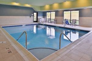 Una piscina interior con agua cristalina, un trampolín y una zona de estar con sillas y una mesa.