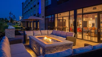 An outdoor seating area with a fire pit, cushioned seating, and a glass-enclosed dining space.