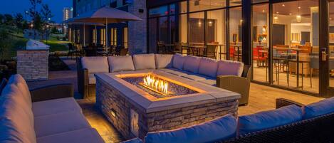 An outdoor seating area with a fire pit, cushioned seating, and a glass-enclosed dining space.