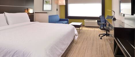 Habitación de hotel con una cama grande, un escritorio, dos sillas, un televisor y una ventana con persianas.