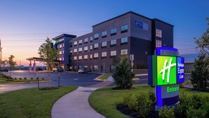 A Holiday Inn Express building with a clear sky, a parking lot, and a sign indicating the entrance. - Holiday Inn Express & Suites Olathe West by IHG (Olathe)