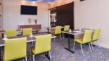 Un salón de conferencias con mesas y sillas, un televisor de pantalla plana y un jarrón decorativo con flores.