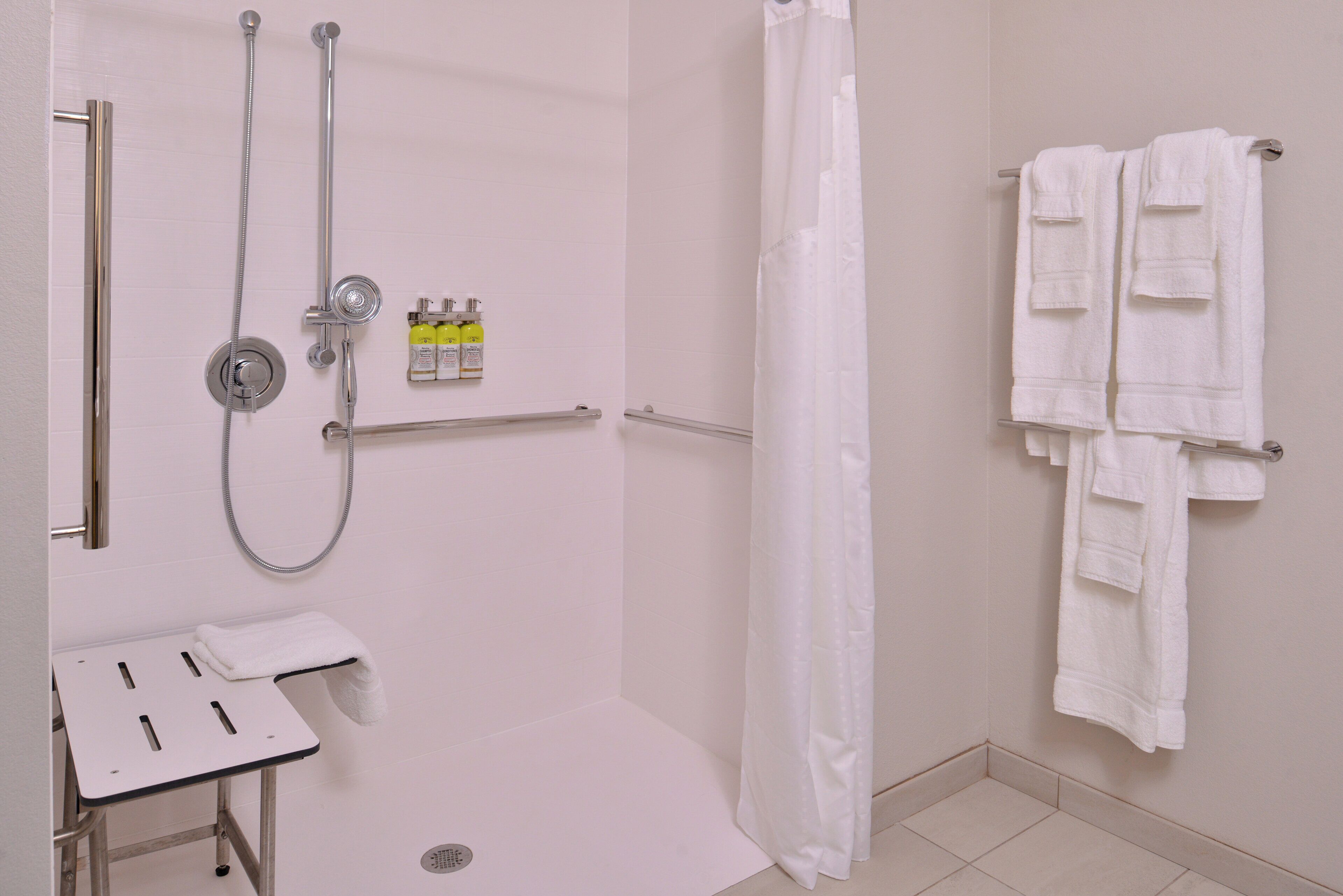A shower area with a glass door, a towel rack with multiple towels, and a small table with a towel.