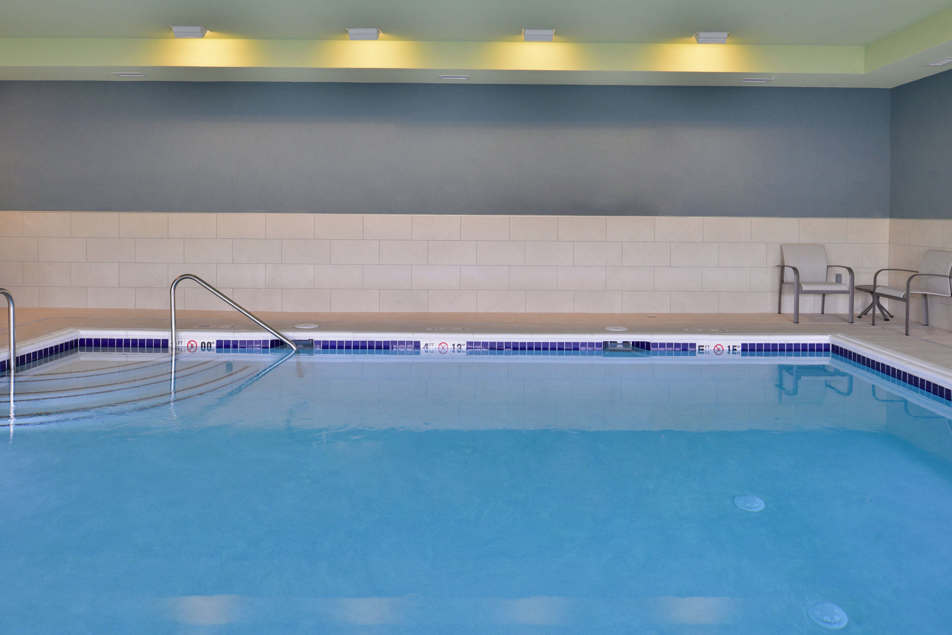Ein Schwimmbecken mit Metallleiter, gefliesten Wänden und einigen Stühlen.