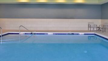 Ein Schwimmbecken mit Metallleiter, gefliesten Wänden und einigen Stühlen.