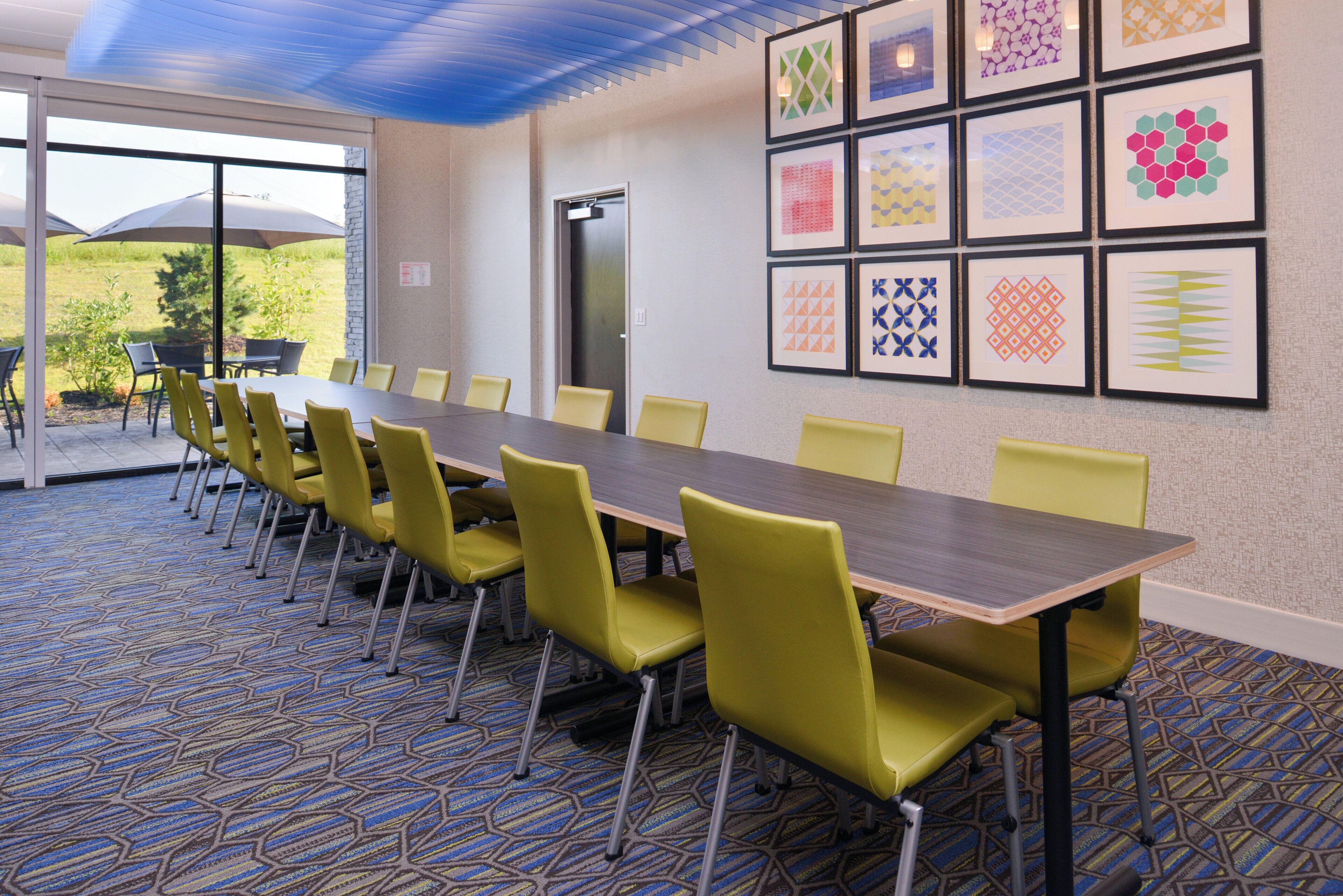 A conference room with a long table and yellow chairs, a patterned carpet, and framed artwork on the walls.