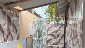 A bathroom with a marble wall, a shower curtain with a leaf pattern, a green artificial grass floor, and a wooden bench.