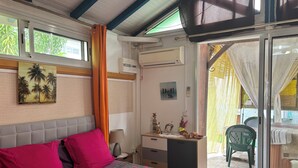A bedroom with a bed, a desk, and a chair. There is a window with curtains, an air conditioning unit, and a painting on the wall.