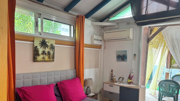 A bedroom with a bed, pillows, a nightstand, a desk, a chair, and a window with curtains.