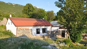 A stone house with a red roof, surrounded by greenery and a mountainous backdrop. - House Sandra (Stokici)