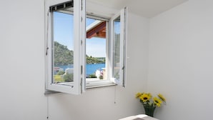 A bedroom with a large window, a bed, and a vase with sunflowers. - Apartments Glorija (Rogoznica)