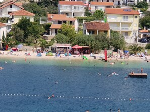 Eine Küstenstadt mit Strand, Gebäuden mit roten Dächern und einem 'PASTO'-Schild.